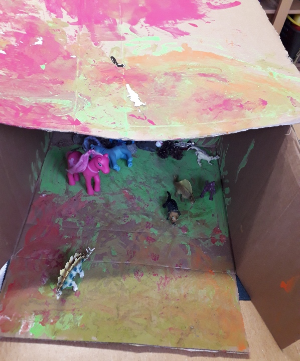 Lasten koristelema pahvilaatikko, jonne dinosaurusmaailma rakentuu
