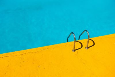 Turkoosiin uima-altaan veteen johtavat tikkaat keltaiselta reunalta.