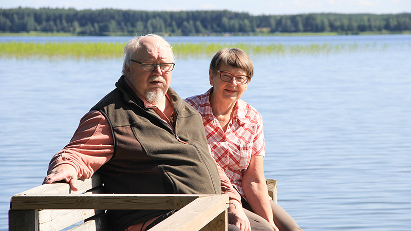 Esko Päivinen ja Leila Kontkanen lähikuvassa laiturilla, taustalla sininen järvi.