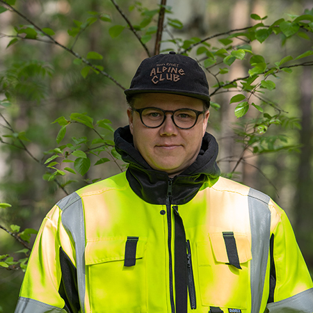 Lauri Kontkanen neonvihreissä huomiovaatteissa poseeraa hymyillen taustallaan vihreää metsää.