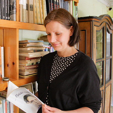 Nainen lukemassa runokirjaa suurten kirjahyllyjen vieressä