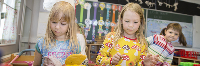 Esiopetuksen lapsia puuhailemassa jotakin pöydän ääressä värikkäässä luokkaympäristössä.