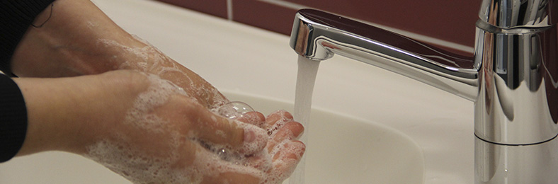 Lähikuvassa näkyvät kädet, joita pestään vaahtoavalla pesuaineella hanan alla.
