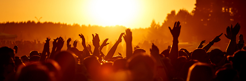 Väkijoukko laskevan auringon punaisessa hehkussa, osa heiluttaa käsiä ilmassa.