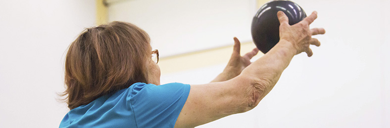 Nainen sinisessä paidassa heittämässä palloa liikuntasalissa