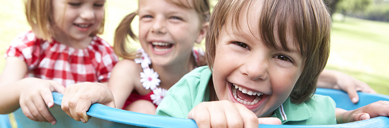 Kolme lasta hymyilemässä ja leikkimässä ulkona