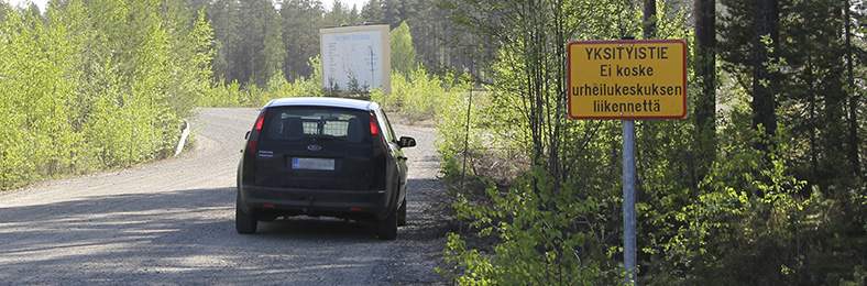Yksityistien liikennemerkin vieressä auto, ympärillä metsämaisemaa.