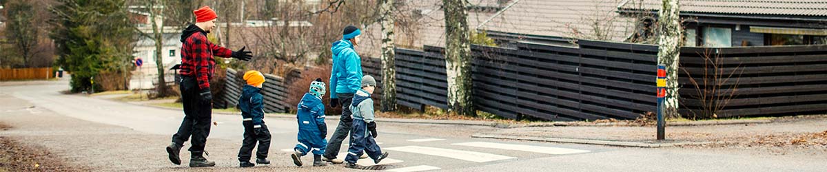 Aikuiset opastavat lapsia ylittämään tien suojatietä pitkin.
